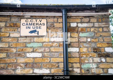 CCTV-Warnschild mit schwarzem Text auf orangem Hintergrund und Kamerasymbol, an der Seite eines Ziegelgebäudes angebracht, um die Überwachung in Betrieb zu halten. Stockfoto