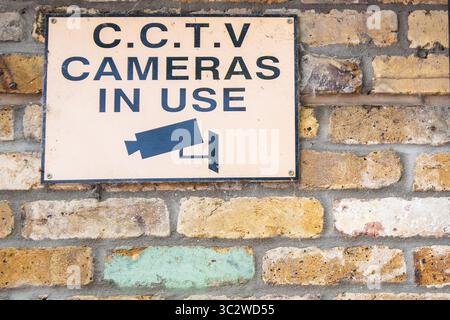 CCTV-Warnschild mit schwarzem Text auf orangem Hintergrund und Kamerasymbol, an der Seite eines Ziegelgebäudes angebracht, um die Überwachung in Betrieb zu halten. Stockfoto