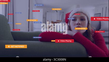 Eine gelehnte Frau trägt einen roten Weihnachtsmütze-Pullover auf der grünen Couch zu Hause, mit Benachrichtigungen, Kopierraum Stockfoto