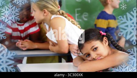Ein Mädchen mit Flechten, das am Schreibtisch des Klassenzimmers mit Schneeflocken-Grafiken und Kopierraum liegt Stockfoto