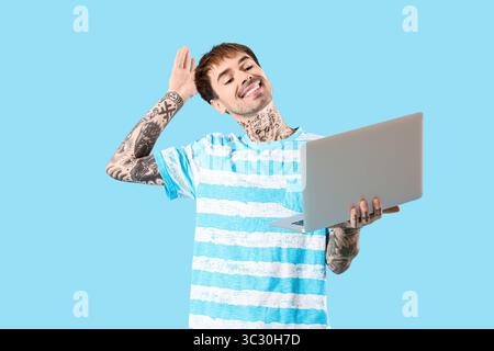 Glücklicher junger Mann mit modernem Laptop, der Hand auf blauem Hintergrund winkt Stockfoto