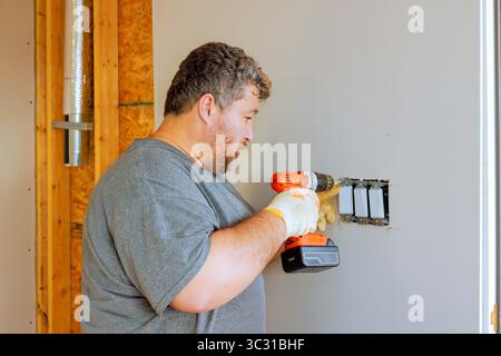 Elektriker-Mann verwendet Bohrmaschine, um Steckdosen an der Wand in einem neuen Haus zu installieren. Stockfoto