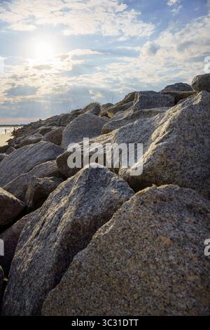 Sonnenlicht, das während der goldenen Stunde durch Wolken über großen Küstenfelsen an einem Strand bricht. Stockfoto