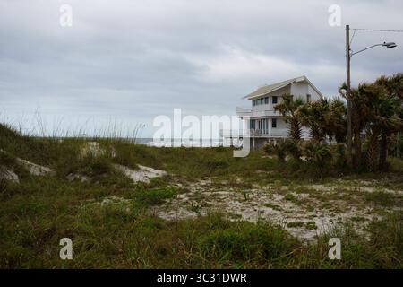 Modernes Strandhaus mit Palmen mit Blick auf das Meer unter bewölktem Himmel. Stockfoto