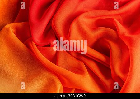 Kräftiges, leuchtendes Orange aus Seidenstoff. Weiche Wellen aus Seidenvorhängen in Herbstfarbe. Die Textur des Seidenstoffs ist in saftigen Rot- und Orangetönen gehalten. Stockfoto