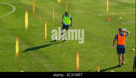 Tropfendes gelbes Lätzchen, das den Fußball auf dem Rasen steuert, mit orangefarbenen und grünen Kegeln Stockfoto