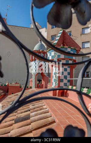 Blick von der Dachterrasse auf die Türme der Casa Vicens durch kunstvoll verzierte Schmiedeeisen mit Gaudi-Moderne-Details. Ikonische Kacheltürme, Schachbrettmuster Stockfoto