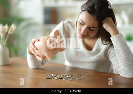 Frustrierte Frau, die zu Hause Geld von der Sparkasse eincheckt Stockfoto