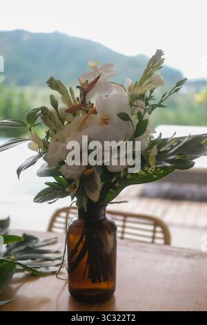 Eine Glasvase mit tropischen Blumen steht auf dem Tisch vor dem Hintergrund der Berge Stockfoto