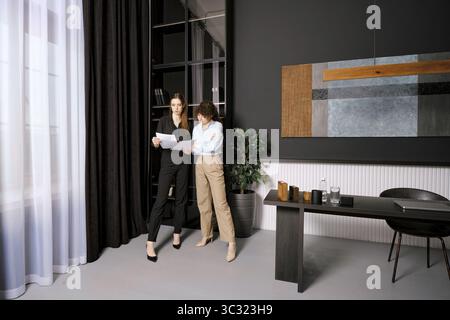 Zwei professionelle Frauen diskutieren in einem stilvollen Büro, während sie Dokumente prüfen Stockfoto