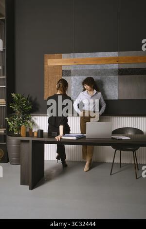 Zwei Frauen diskutieren über ihre Arbeit in einem modernen Bürobereich mit eleganter Einrichtung und stilvollen Möbeln Stockfoto