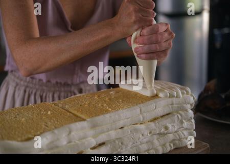 Nahaufnahme der Hände einer jungen Konditorin, die einen großen Geburtstagskuchen zubereitet Stockfoto