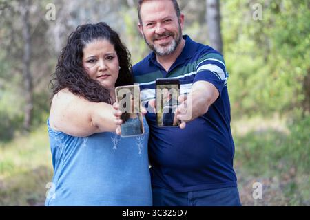 Ein Mann und eine Frau halten ihre Handys hoch, um ein Selfie zu machen. Der Mann trägt ein blaues Hemd und die Frau ein blaues Tanktop. Szene ist Stockfoto