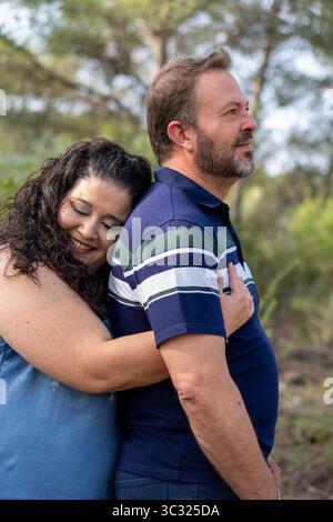 Ein Mann und eine Frau umarmen sich in einem Wald. Der Mann trägt ein blau gestreiftes Hemd Stockfoto