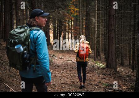 Wandergruppe mit Outdoor-Ausrüstung und Sportbekleidung, die durch den dunklen Wald spazieren Stockfoto