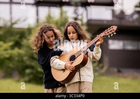 Zwei Zwillingsmädchen mit lockigem Haar spielen auf einer Gitarre und haben Spaß Stockfoto