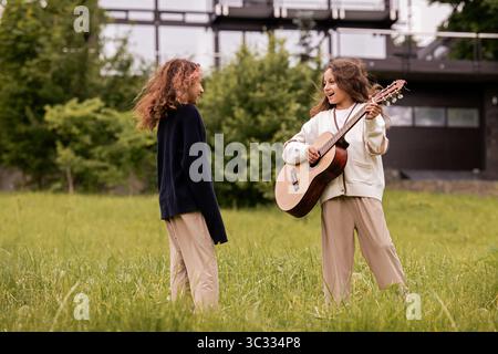 Zwei Zwillingsmädchen mit lockigem Haar spielen auf einer Gitarre und haben Spaß Stockfoto