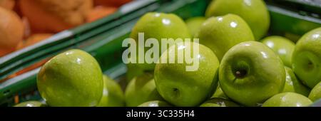 Nahaufnahme von grünen Äpfeln in einer Plastikkiste, fotografiert auf einem Markt oder Lebensmittelgeschäft. Die Äpfel sind glänzend und frisch, mit subtilen Reflexen. Stockfoto