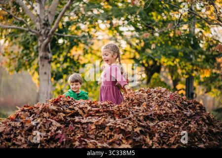 Aufregende Kinder, die in einem Herbstlaub im Park spielen Stockfoto