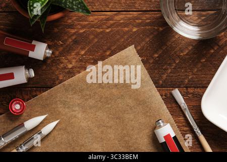 Vorbereitung auf das Zeichnen. Tuben aus Acrylfarbe, Pinsel, ein Glas Wasser auf dunklem hölzernem Hintergrund. Ein Ort für Ihre SMS. Stockfoto