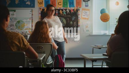 Lehrerin, die Unterricht für Schüler der Grundschule im modernen farbenfrohen Klassenzimmer durchführt. Kluge, vielfältige Kinder sitzen an Schreibtischen, studieren Ökologie, hören Lehrern zu. Stockfoto