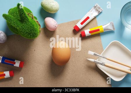 Ostereier Dekoration und kreative Zubereitung. Ein Pappblatt auf blauem Hintergrund mit braunen Eiern, Pinseln und Tuben. Stockfoto