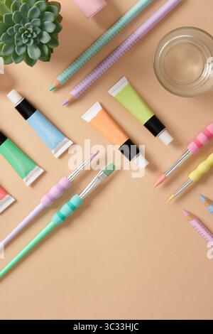 Karte mit Kunstzubehör in grünen, gelben, rosa und lila Pastellfarben auf beigefarbenem Hintergrund. Farben, Farbstifte und Pinsel. Platz für Ihren Text Stockfoto