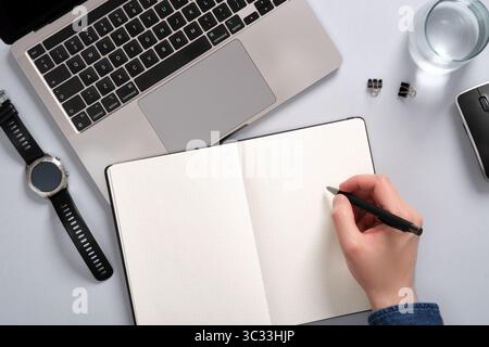 Schreibtisch mit Computer, Notizblock, Schreibzubehör. Die Hand eines Mannes, der in einen Notizblock schreibt. Ein Ort für Ihre SMS. Stockfoto