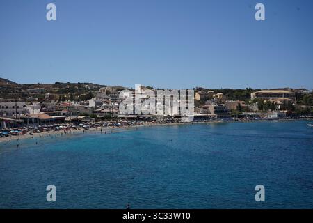 Der Strand von Agia Pelagia auf Kreta, Griechenland - Blick vom Hotel. Sandstrand mit klarem, türkisfarbenem Wasser. Leute, die sich unter bunten Sonnenschirmen sonnen. Stockfoto