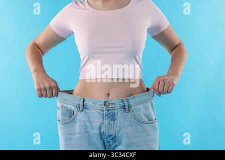 Frau trägt alte Jeans nach Gewichtsverlust auf hellblauem Hintergrund, Nahaufnahme Stockfoto