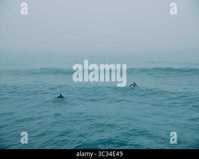 Zwei Surfer warten auf eine Welle in einer leeren blauen Meereslandschaft Stockfoto