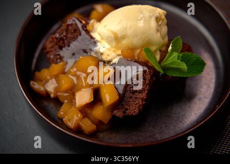 Köstliche Schokoladen-Brownie-Delight mit Vanillla-Eis und frischem Fruchtkompott, perfekt serviert auf einem dunklen Teller Stockfoto