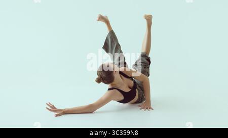 Zeitgenössische Tänzerin, die sich auf dem Boden dreht, beide Beine angehoben und der Blick zur Seite gedreht Stockfoto
