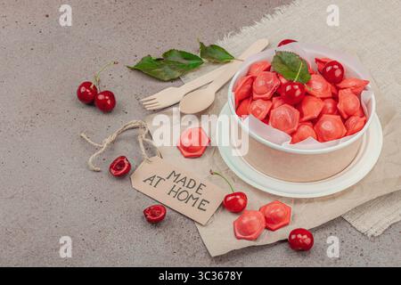 Gefrorene Kirschknödel in einer Papierschale, flache Lagenkomposition mit frischen Kirschen, Minze, handgefertigtes Etikett. Zero Waste Konzept der Lebensmittellieferung, Smart Co Stockfoto