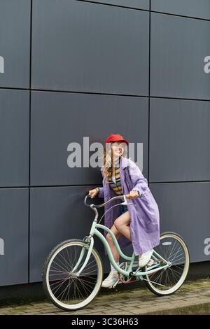 Eine fröhliche junge Frau, die für den Sommer gekleidet ist, lehnt sich auf ihr Fahrrad und lächelt vor einem eleganten Hintergrund. Stockfoto