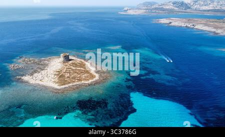 Blick auf den antiken Wachturm aus Stein am Strand La Pelosa, Stintino, Sardinien. Isola Piana und Asinara im Hintergrund unter einem hellen Sommerhimmel. Stockfoto