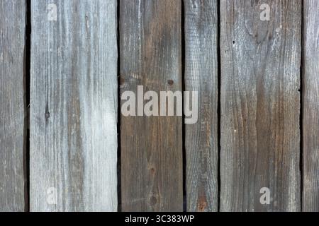 Nahaufnahme eines verwitterten Holzzauns mit vertikalen Dielen, die natürliche Holzmaserung und Textur in Grau- und Brauntönen zeigen. Stockfoto