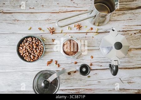 Arbeitsbereich für aromatischen Kaffee: Ganze Bohnen, gemahlene arabica-Bohnen, Mokakanne, Handmahlmaschine und Stahlkanne auf rustikalem Holz, helles Tageslicht Rahmen für ein langsames selbstgebrühtes Bier Stockfoto