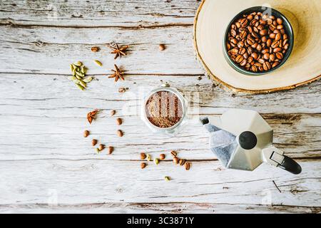 Rustikales Kaffee-Stillleben: Gemahlene arabica, Mokakanne und Schüssel Bohnen auf roher Holzscheibe mit verstreuten Gewürzen, gemütliches Herbstcafé-Flair und jede Menge Kopie sp Stockfoto