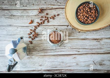 Komposition aus Mokakanne, gemahlenen und ganzen Kaffeebohnen mit verstreuten Gewürzen, die diagonale Strömung auf hellem rustikalem Holz bilden, helle Küche atmosp Stockfoto