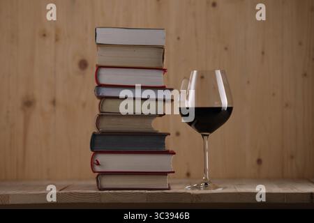 Ein Glas Rotwein und stapelbare Bücher auf einem Holztisch Stockfoto