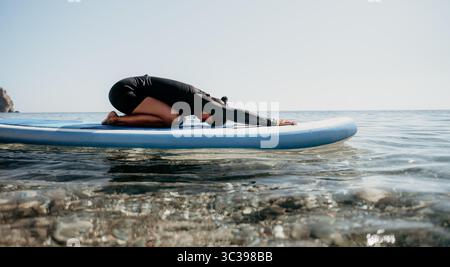 Yoga Paddleboard Wasser - Person übt Yoga auf dem Paddleboard im Wasser. Stockfoto