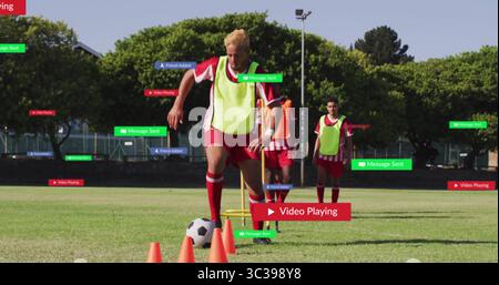 Tropfender Mann in gelbem Lätzchen, der den Fußball durch orangefarbene Kegel auf dem Feld führt, mit digitalen Etiketten Stockfoto