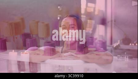 Eine Frau, die Badeanzug in der Badewanne im Spa-Raum trägt, mit Kerzen, Handtüchern, Fenster, Pflanze Stockfoto