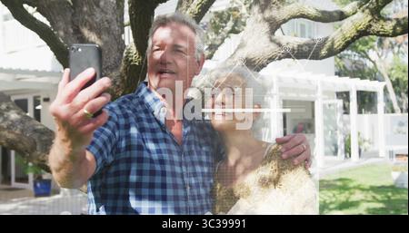 Selfie, Pullover-bekleidete Frau und karierter Mann unter Eiche im Garten, mit Smartphone Stockfoto