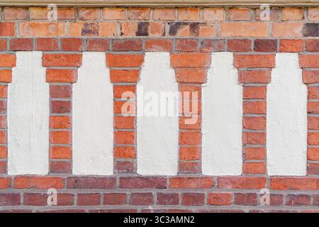 Weiße, flaschenförmige Silhouetten, gemalt auf einer roten Ziegelwand. Sich wiederholende Muster und strukturierter Kontrast zwischen Farbe und Mauerwerk. Stockfoto
