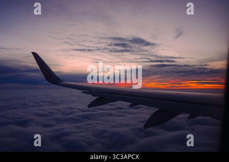 Blick auf den Flugzeugflügel in großer Höhe über Wolken bei lebendigem Sonnenuntergang oder Sonnenaufgang Stockfoto