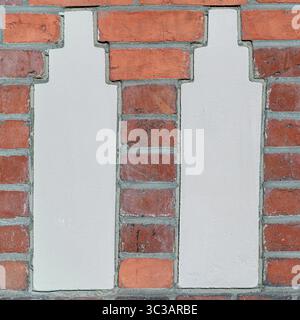 Eine detaillierte architektonische Nahaufnahme zeigt zwei vertikal ausgerichtete weiße Putzeinlagen, die von roten Ziegeln eingerahmt sind. Stockfoto
