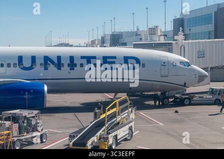 United Airlines 737 parkte an einem Flughafentor und verladete an einer Jetbrücke mit Bodenbesatzung und Fahrzeugen in der Nähe. Stockfoto