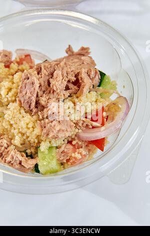 Eine köstliche gesunde Mahlzeit aus Thunfisch, Couscous und frischem Gemüse, serviert in einer klaren Plastikschale, perfekt für ausgewogene Ernährung und schnelles Essen Stockfoto
